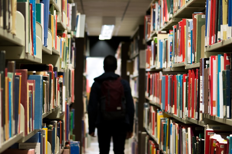 A student walking through library book stacks, viewed from behind
