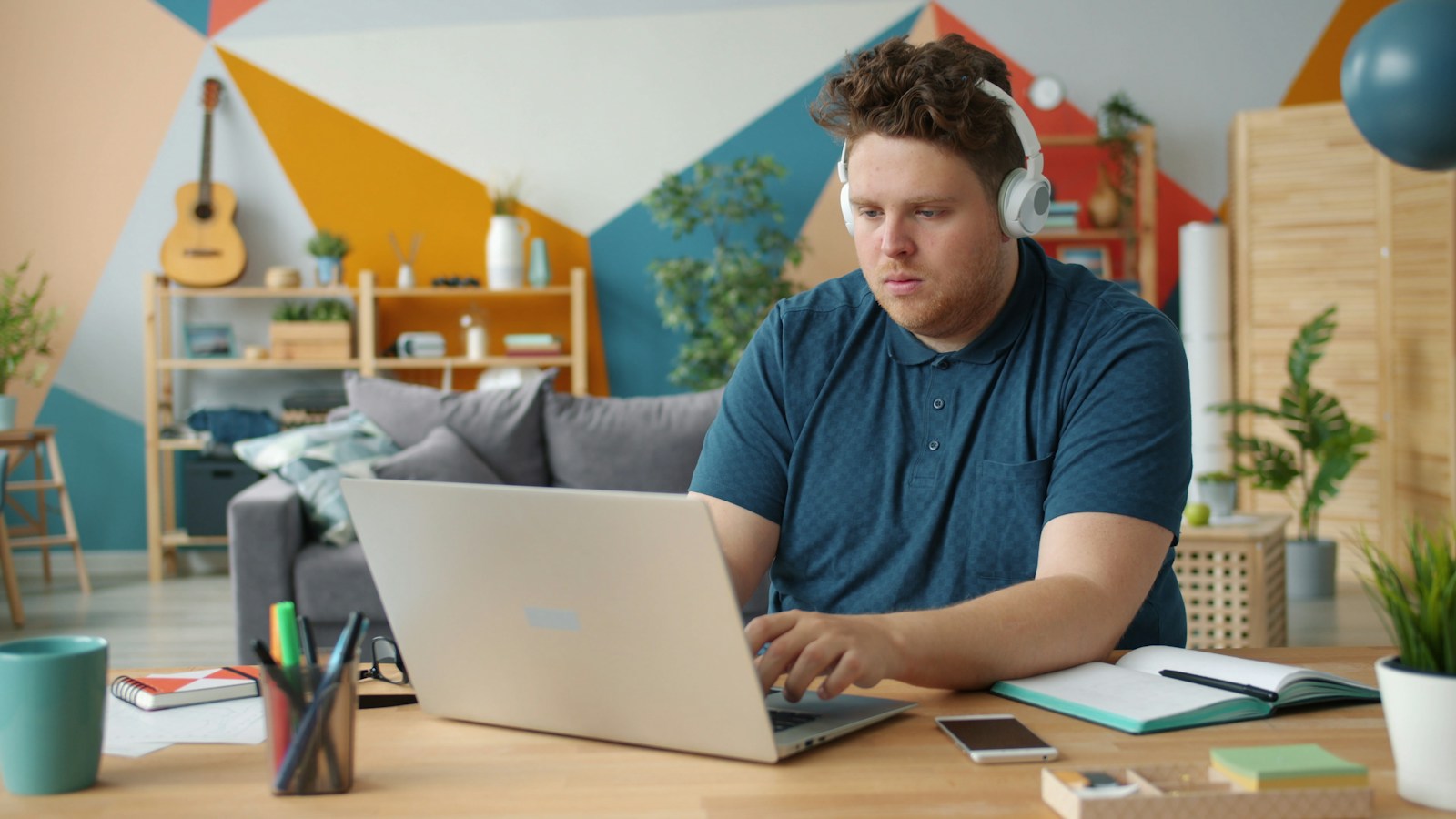 Student in headphones working on a laptop at a desk with an open notebook